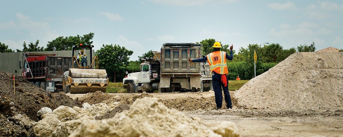 A worker assists in backing up a truck unloading limestone