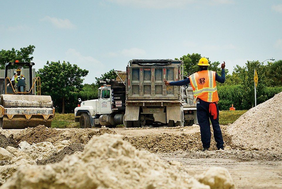 A worker assists in backing up a truck unloading limestone